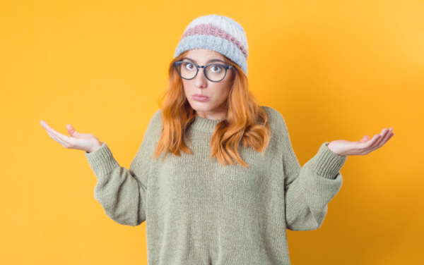 Confused young woman, isolated on white background being in confusion while shrugs shoulders.