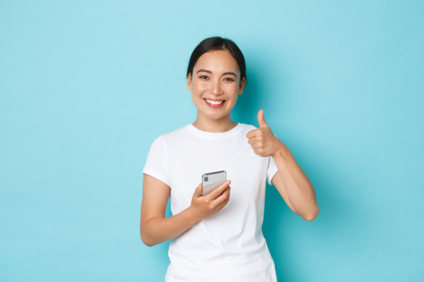 Woman giving a thumbs-up while holding a mobile phone.