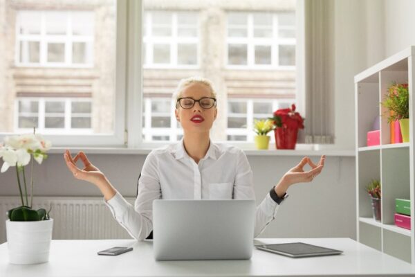 A woman sits quietly meditating in a tranquil office space.