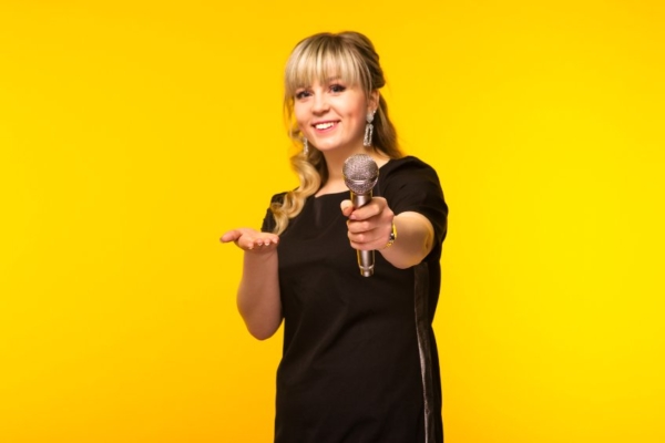 Woman holding a microphone inviting the viewer to speak.