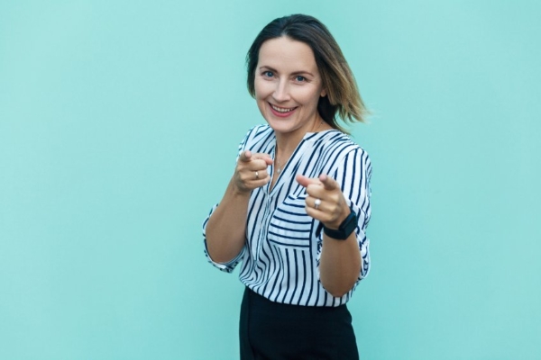 A woman wearing business clothing smiling confidently pointing at your, the viewer.